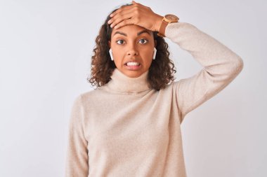 İzole edilmiş beyaz arka planda kablosuz kulaklık kullanarak müzik dinleyen Brezilyalı bir kadın. Elleri başının üstünde, utanç ve şaşkınlık dolu, sinirli ve hayal kırıklığına uğramış bir halde. Hata için korku ve üzüntü.