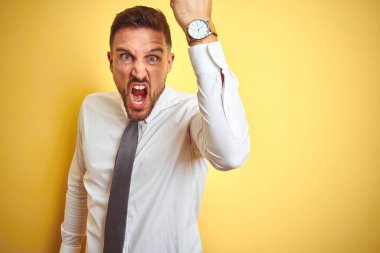Sarı arka plan üzerinde zarif beyaz gömlek giyen genç yakışıklı iş adamı öfkeyle bağırırken kızgın ve kızgın bir şekilde yumruk kaldırıyor. Öfke ve agresif kavram.