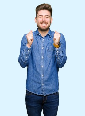 Genç yakışıklı sarışın adam rahat kot gömlek kolları olan başarı için heyecanlı zafer kutluyor gülümseyen kaldırdı. Kazanan kavramı.