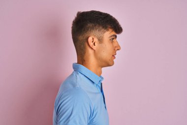 Mavi polo giyen genç Hintli adam izole edilmiş pembe arka planda duruyor. Yan tarafa bakıyor, rahat poz veriyor, kendine güvenen bir gülümsemesi var..