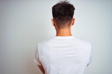 Asyalı genç bir Çinli tişört giyiyor. İzole edilmiş beyaz arka planda duruyor. Arkaya bakıyor ve kollarını kavuşturuyor.