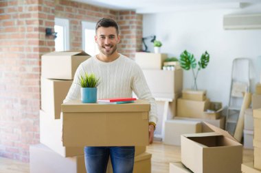 Yeni dairede karton kutu tutan yakışıklı adam, yeni bir eve hareket çok mutlu gülümseyen