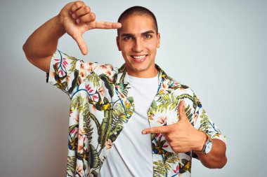 Tatilde, beyaz arka planda Hawaii tişörtü giymiş, gülümseyen, elleri ve parmakları mutlu yüzlü genç yakışıklı bir adam. Yaratıcılık ve fotoğrafçılık kavramı.