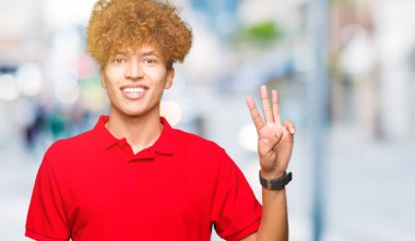 Gösterilen ve parmakları ile işaret kırmızı t-shirt giyen afro saçlı Genç yakışıklı adam kendinden emin ve mutlu gülümseyerek iken üçüncü.