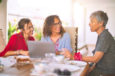 Orta yaşlı kadınlarla buluşup, öğle yemeği yiyip, kahve içiyorlar. Olgun arkadaşlar, güneşli bir günde evde dizüstü bilgisayar kullanarak mutlu bir şekilde gülümserler.