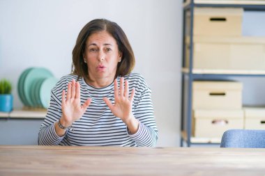 Evde masada oturan orta yaş yaşlı kadın korku ve ifade ile reddi ve inkar gösteren avuç içi uzak hareket. Dur ve yasak.