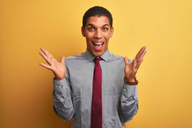 Genç yakışıklı Arap iş adamı gömlek ve kravat takıp izole edilmiş sarı arka planda çılgın ve başarıyı kollarını kaldırıp heyecanla haykırarak kutluyor. Kazanan konsept