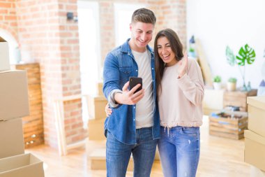 Beautiful young couple moving to a new house using smartphone very happy and excited, winner expression celebrating victory screaming with big smile and raised hands