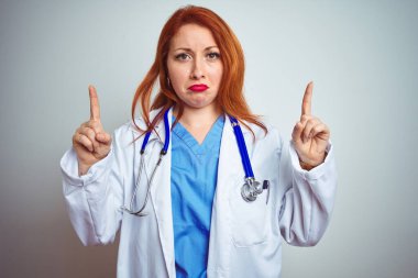 Genç kızıl saçlı kadın steteskop kullanıyor. İzole edilmiş beyaz arka plan üzerinde. Üzgün ve üzgün görünüyor..