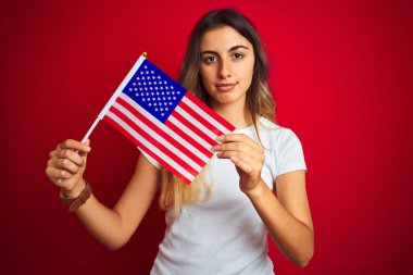 Amerika Birleşik Devletleri bayrağını kırmızı izole edilmiş arka planda tutan genç bir kadın.