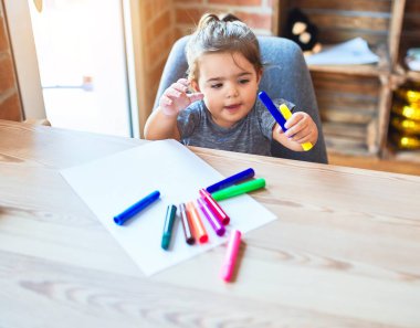Anaokulunda renkli kalemlerle çizim yapan güzel bir çocuk.