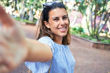 Yeşil Park 'ta mutlu ve neşeli gülümseyen güzel bir kadın güneşli bir yaz gününde akıllı telefon kullanarak selfie çekiyor.
