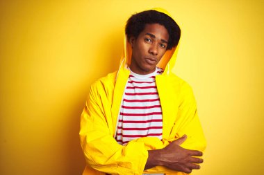 Afro saçlı, kapüşonlu bir Afrikalı adam izole edilmiş sarı arka plan üzerinde duruyor şüpheci ve gergin, yüzünde çapraz kollarla onaylamayan bir ifade var. Negatif kişi.