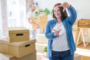 Genç çift yeni bir eve taşınıyor, artı evde gülümseyen bir kadın elleri ve parmakları mutlu yüzlü bir çerçeve yapıyor. Yaratıcılık ve fotoğrafçılık kavramı.