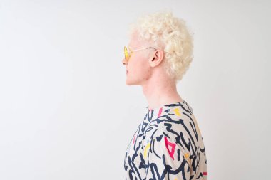 Renkli tişört ve güneş gözlüğü takan genç albino bir adam izole edilmiş kırmızı arka plan, rahat profil pozu, kendine güvenen bir gülümsemeyle doğal bir poz..