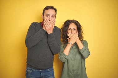 Soyutlanmış sarı arka planda güzel bir orta yaşlı çift yanlışlıkla ağızlarını kapatarak şok geçirdiler. Gizli konsept.