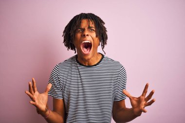 Rasta desenli tişörtlü Afro adam pembe arka planda dikiliyor. Deli gibi bağırıyor ve agresif bir ifade ve kolla bağırıyor. Hayal kırıklığı konsepti.