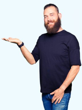 Neşeli sunulması ve kameraya bakarak avucunun ile işaret gülümseyen rahat t-shirt giyen genç sarışın adam.