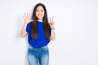 Güzel esmer kadın, izole edilmiş arka planda 7 numaralı parmaklarıyla gülümseyerek kendinden emin ve mutlu bir şekilde görünüyor..