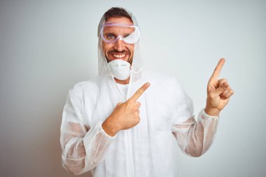 Profesyonel işçi teçhizatı takan ressam izole edilmiş arka planda gülümseyerek kameraya bakıyor ve iki eliyle ve parmaklarıyla kenarı işaret ediyor..