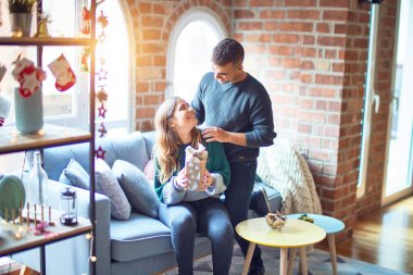 Mutlu ve kendinden emin gülümseyen genç bir çift. Evde Noel süslemeleri yapan sürpriz bir kadın var.