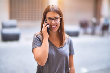 Mutlu ve kendinden emin gülümseyen genç ve güzel bir kadın. Yüzünde gülümsemeyle kasaba caddesinde akıllı telefonun başında konuşmak.
