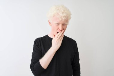 Siyah tişörtlü genç albino adam izole edilmiş beyaz arka planda dikiliyor. Elle ağzını kapatmaktan sıkılmış. Huzursuz ve uykulu..