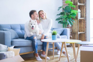 Karton kutular etrafında yeni evde kanepede oturan köpek ile genç güzel çift