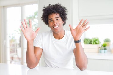 Genç Afro-Amerikalı adam, günlük beyaz tişörtler giyip evinde oturuyor ve parmaklarını on numarayı gösterirken kendinden emin ve mutlu gülümsüyor..