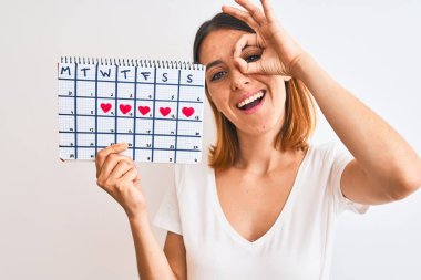 Güzel, kızıl saçlı bir kadın regl takvimini izole edilmiş arka planda tutuyor. Mutlu bir yüzü var. Gülümsüyor.