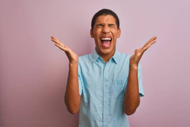 Mavi tişörtlü genç yakışıklı Arap adam, izole edilmiş pembe arka planda duruyor. Kolları havada ve gözleri kapalı heyecanla haykırarak başarının çılgınlığını kutluyor. Kazanan konsept