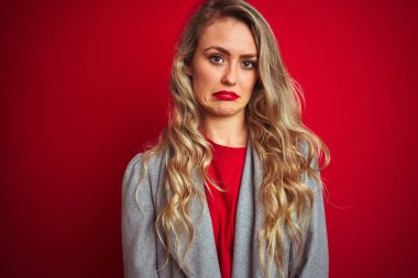 Kırmızının üzerinde duran zarif ceketli genç ve güzel bir iş kadını üzgün ve endişeli, sinirli ve korkmuş. Üzücü ifade.