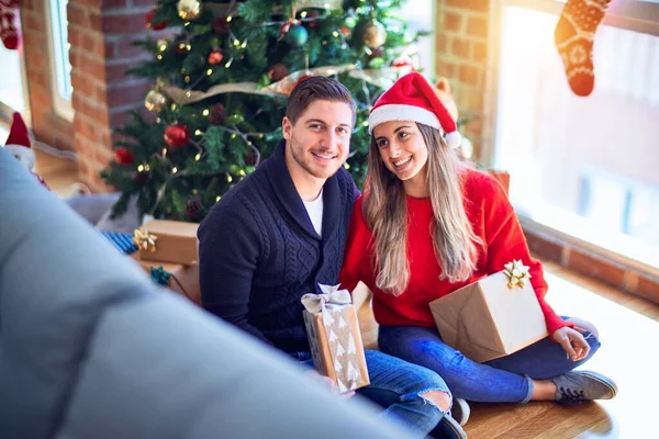 年轻漂亮的夫妇面带微笑 既快乐又自信 在家里 坐在地板上拿着礼物 抱着圣诞树 — 图库照片