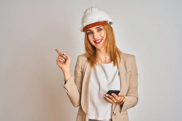 年轻的高加索工程师女人使用智能手机 戴着安全帽 很高兴手指手画脚 — 图库照片