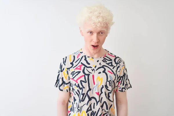 Young albino blond man wearing colorful t-shirt standing over isolated white background afraid and shocked with surprise expression, fear and excited face.