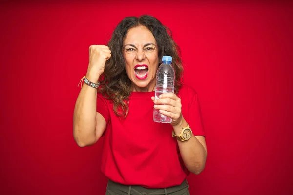 中年妇女拿着塑料水瓶在红色孤立的背景下愤怒地大叫 疯狂地高喊 怒气冲冲 — 图库照片