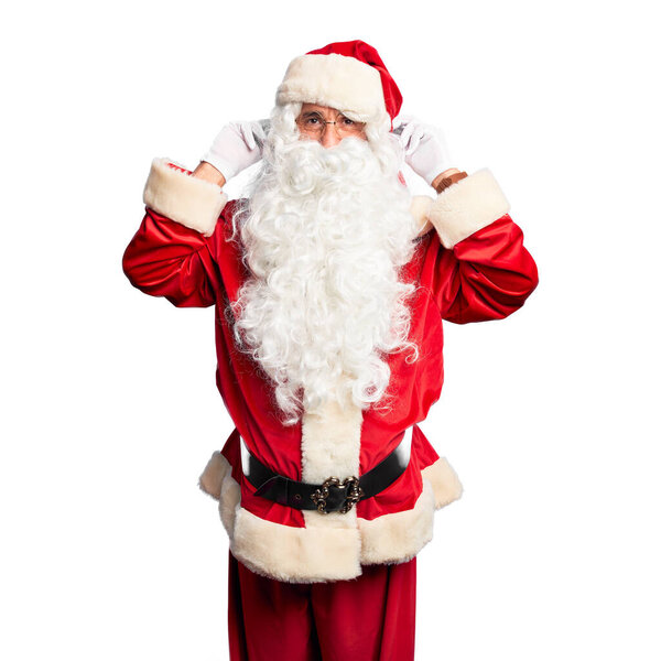 Middle age handsome man wearing Santa Claus costume and beard standing Smiling pulling ears with fingers, funny gesture. Audition problem
