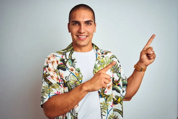 若いですハンサムな男で休日身に着けていますハワイアンシャツ上の白い背景笑顔とカメラを見て2本の手と指で側に指して — ストック写真