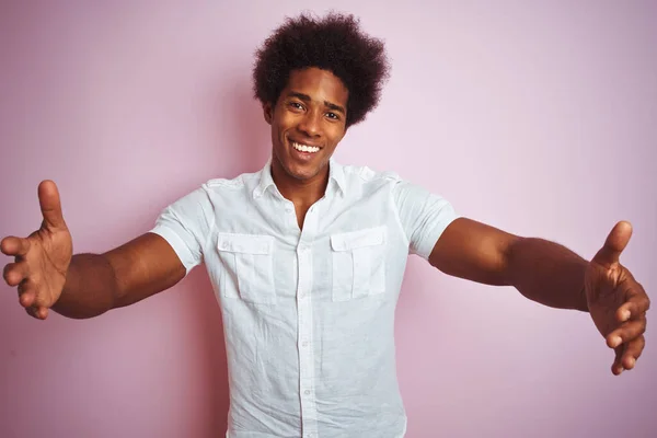 白いシャツを着たアフロの髪をした若いアメリカ人男性が 人見知りのピンクの背景の上に立っている 幸せを受け入れる陽気な表情 — ストック写真