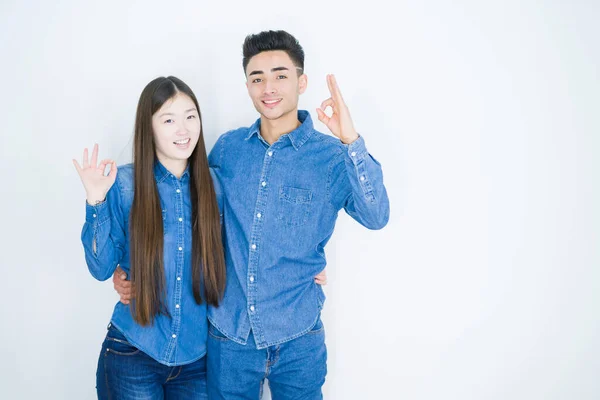 Beautiful young asian couple over white isolated background smiling positive doing ok sign with hand and fingers. Successful expression.