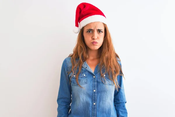孤立した背景にクリスマスの帽子をかぶっている若い美しい赤毛の女性は 面白い顔で頬をむいています 口は空気で膨脹し 狂気の表現 — ストック写真