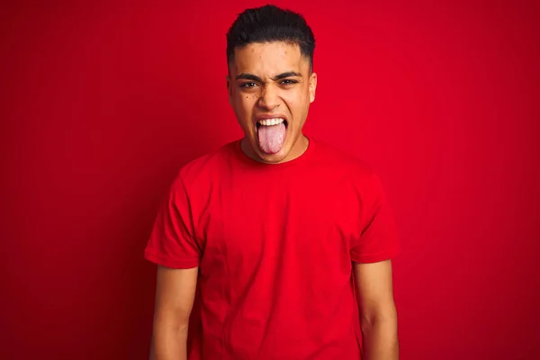 年轻的巴西男子穿着T恤 站在孤立的红色背景上 带着滑稽的表情伸出舌头 情感概念 — 图库照片