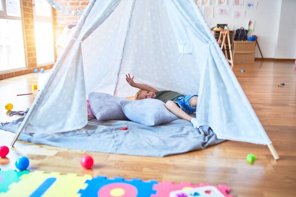 Young caucasian kid playing at kindergarten inside teepee. Preschooler boy happy at playroom with indian tent.
