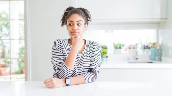 Beautiful african american woman with afro hair wearing casual striped sweater looking confident at the camera smiling with crossed arms and hand raised on chin. Thinking positive.
