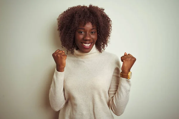 孤立した白い背景にタートルネックのセーターを着た若いアフリカのアフロ女性は 腕を上げて目を開いて成功したことに驚いて驚いて驚いています 勝者のコンセプト — ストック写真
