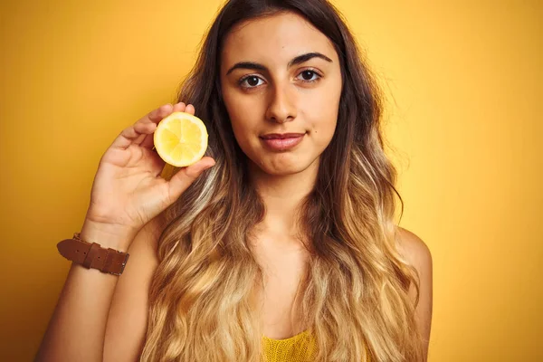 年轻而漂亮的女人 背负着半个柠檬的黄色孤立的背景 聪明的脸上带着自信的表情 严肃地思考着 — 图库照片