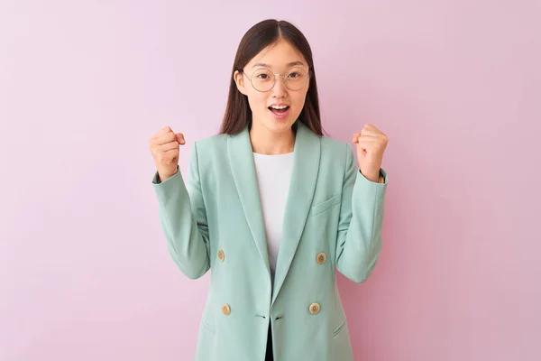 Young chinese businesswoman wearing jacket and glasses over isolated pink background celebrating surprised and amazed for success with arms raised and open eyes. Winner concept.