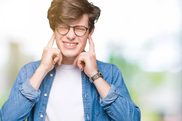 年轻英俊的男子戴眼镜在孤立的背景覆盖耳朵用手指与愤怒的表情大声的音乐的噪音 聋哑人的概念 — 图库照片