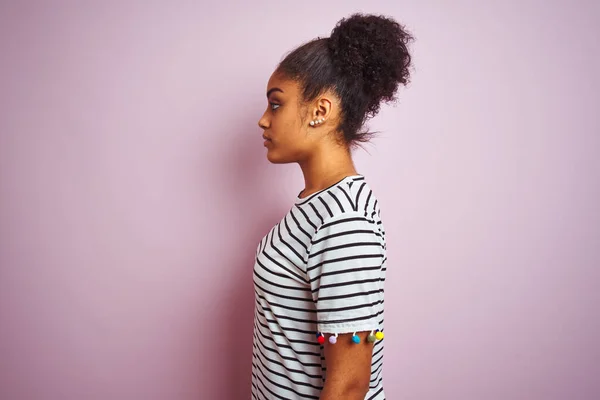 African american woman wearing navy striped t-shirt standing over isolated pink background looking to side, relax profile pose with natural face with confident smile.