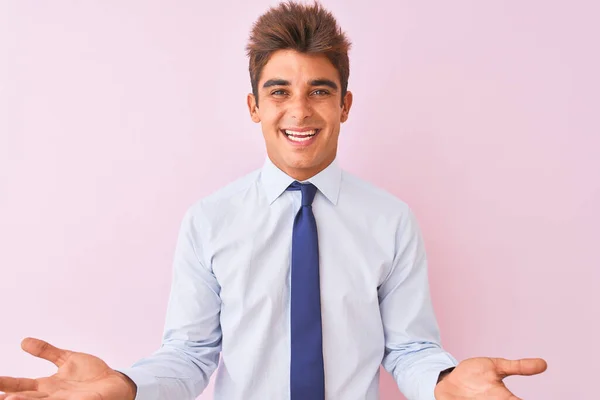 シャツとネクタイを着た若いハンサムなビジネスマンは 友好的な歓迎 肯定的で自信に満ちた挨拶として 開いた腕で陽気な笑顔の孤立したピンクの背景の上に立って — ストック写真
